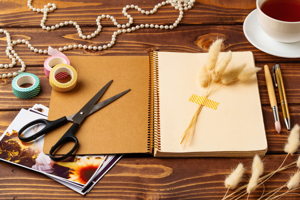 Un espacio de trabajo repleto de materiales de scrapbooking como papeles, tijeras, cinta decorativa y una taza de té.