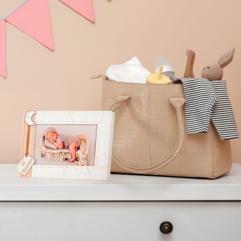 Mother's bag with baby's stuff on white chest of drawers near beige wall. Space for text